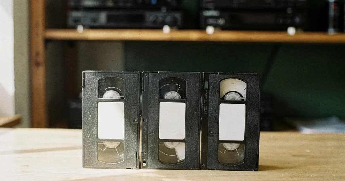 明るい木のカウンターに立てて並べられたビデオテープ3本と、その奥にぼかして写るビデオ機材の棚